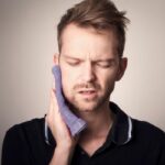 un jeune homme tient une serviette sur sa machoire qui lui fait mal